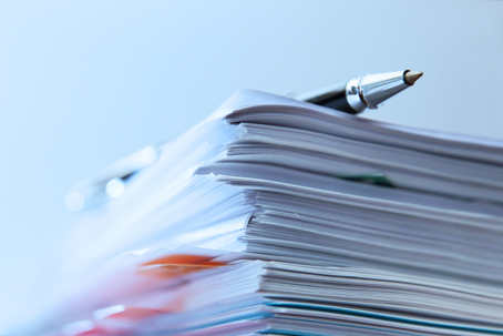 ballpoint pen rests on top of a stack of documents